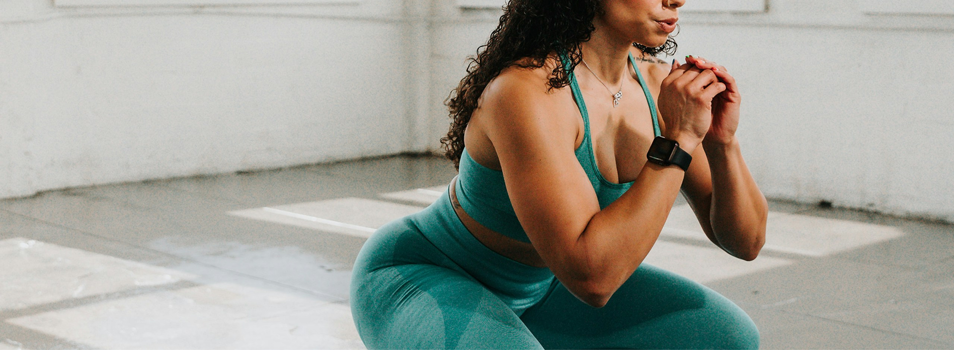 Woman in teal athletic wear sitting on a yoga mat in a studio.